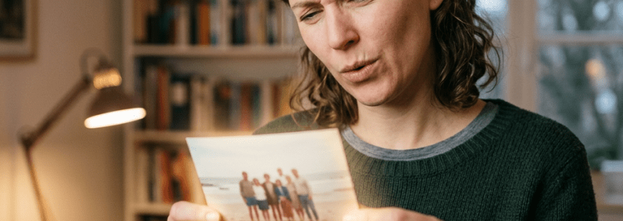 Woman looking thoughtfully at an old photo of a group of people on a beach